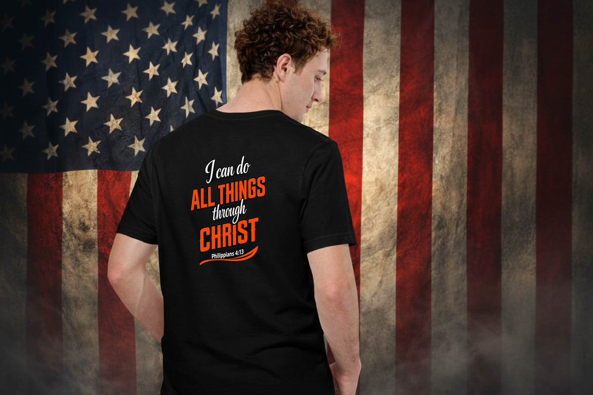 A man shown from behind wearing a black t-shirt with a religious graphic on the back, set against a distressed American flag background.